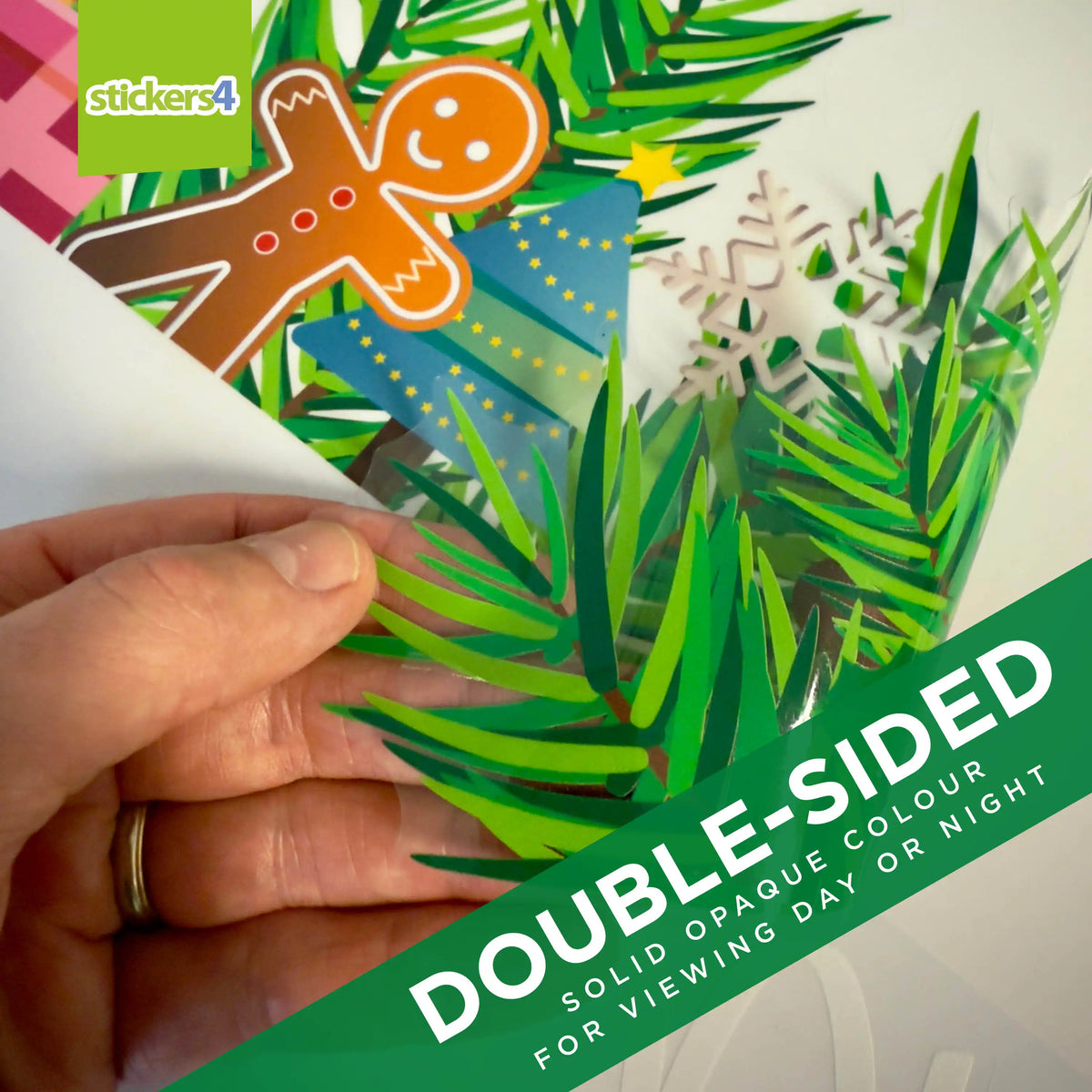 Hand holding a double-sided sticker with a gingerbread man and snowflake design, with text about solid opaque color for day or night viewing.