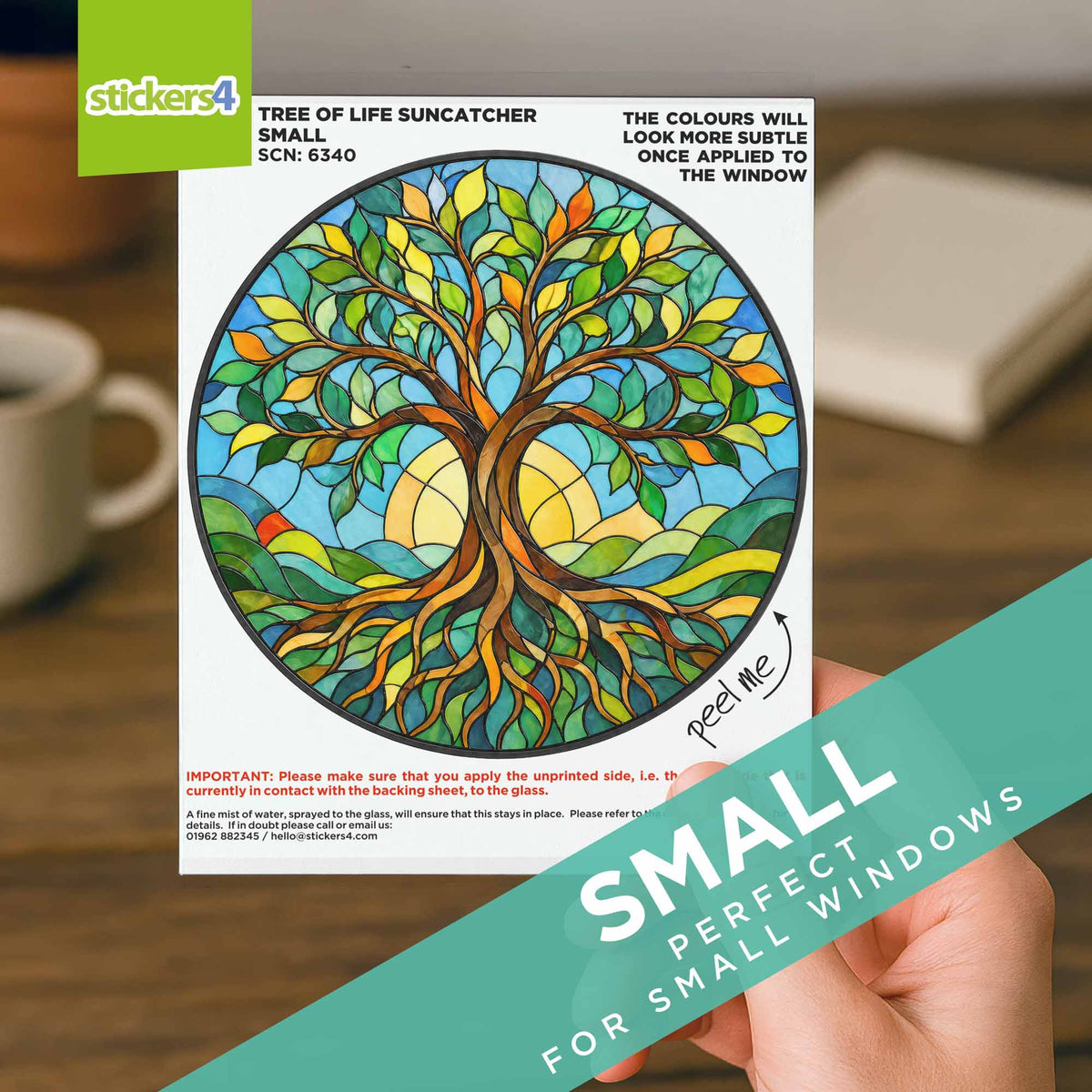 Sticker with a colorful tree design held by a hand, with a cup and book in the background.